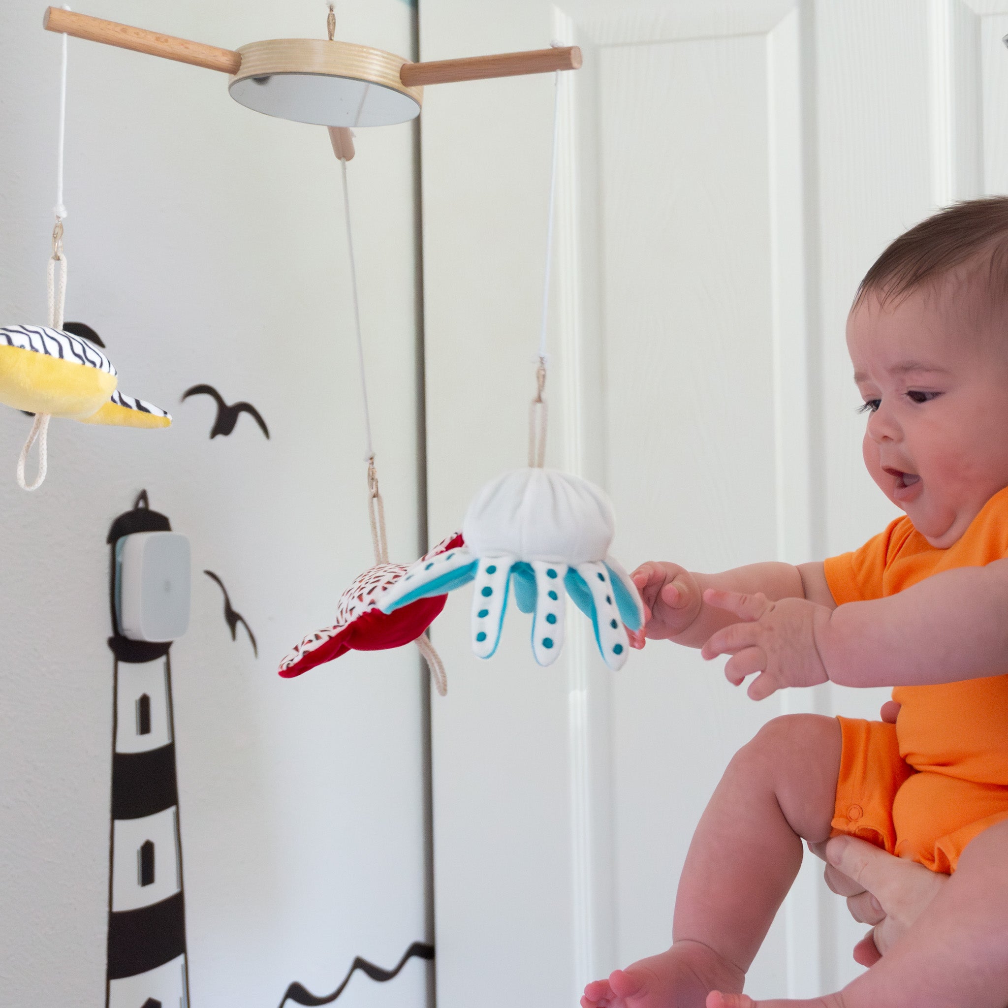 A baby is on the right, grabbing and playing with an octopus plush toy hanging from a mobile.