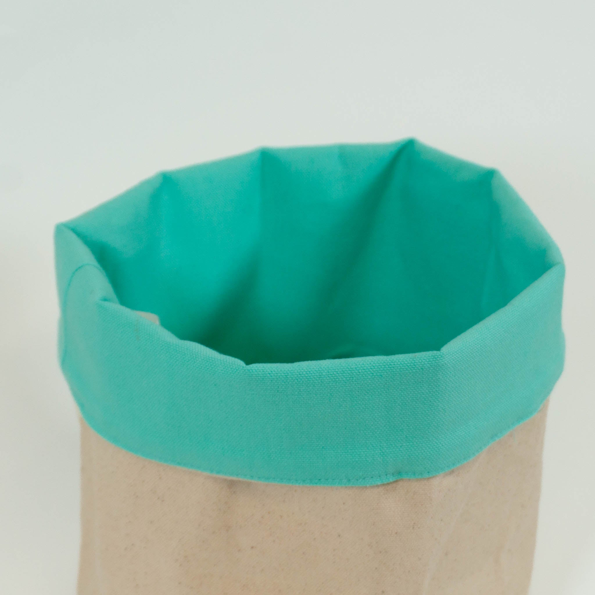 Close up of a cloth storage basket with the rim folded over to show the mint green inside color, with the beige color on the outside. 