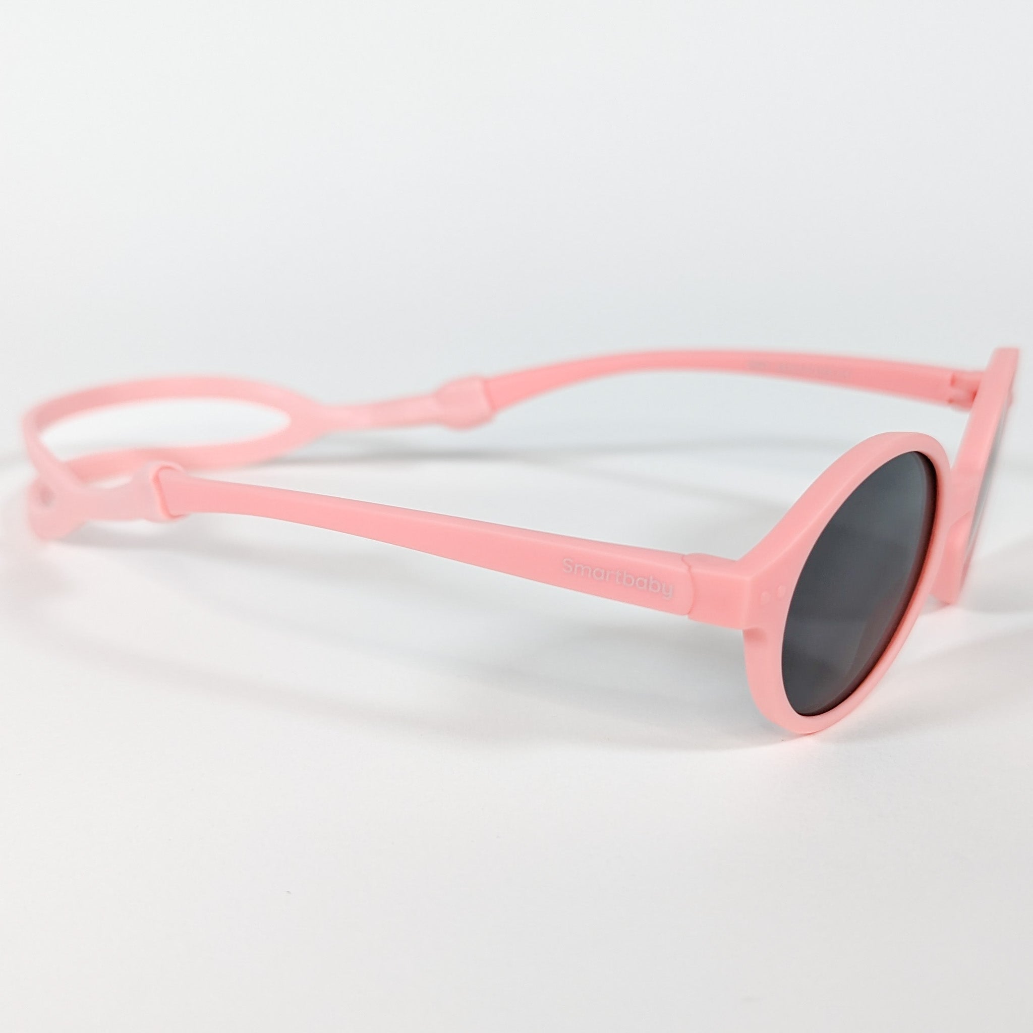 A zoomed in view of the side of a pair of baby sunglasses with a pink frame and a strap.