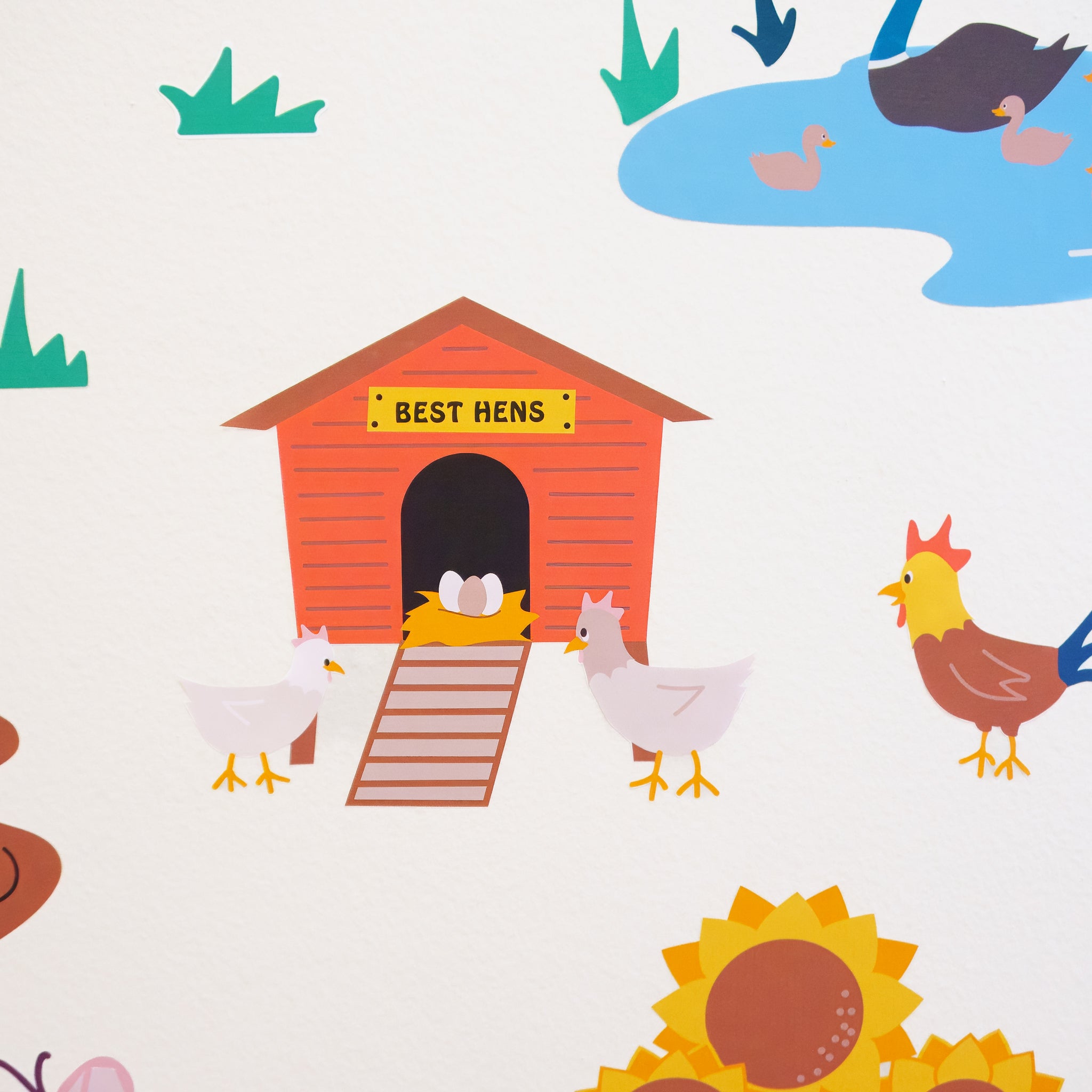 A close up of a wall art decal of a red chicken coop with 3 eggs inside, stairs and 2 hens in front. On the right side is a rooster. There is a sign on the chicken coop reading "Best Hens".