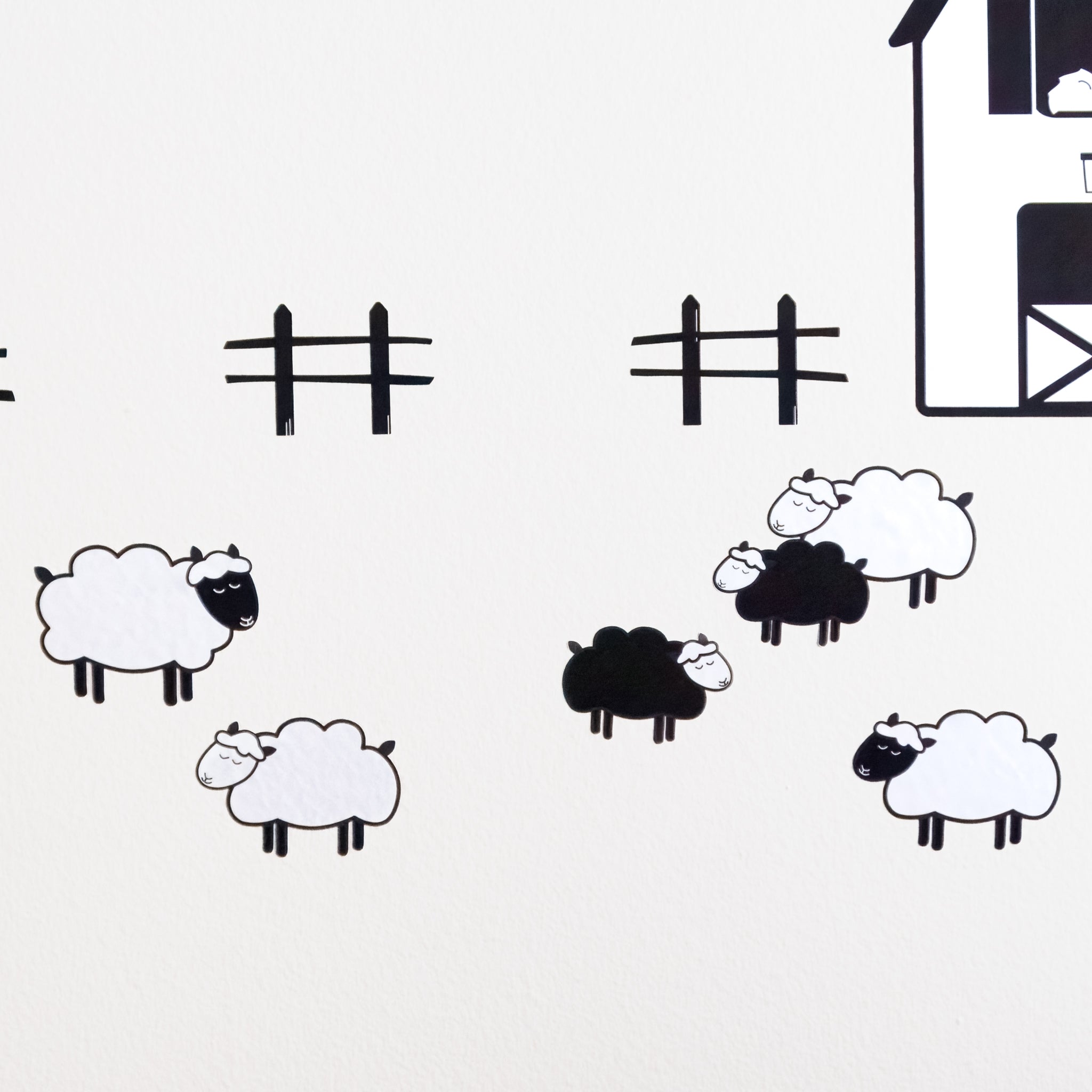 Four white sheep and two black sheep wall art decals on a white wall in front of part of a barn and a few fences.