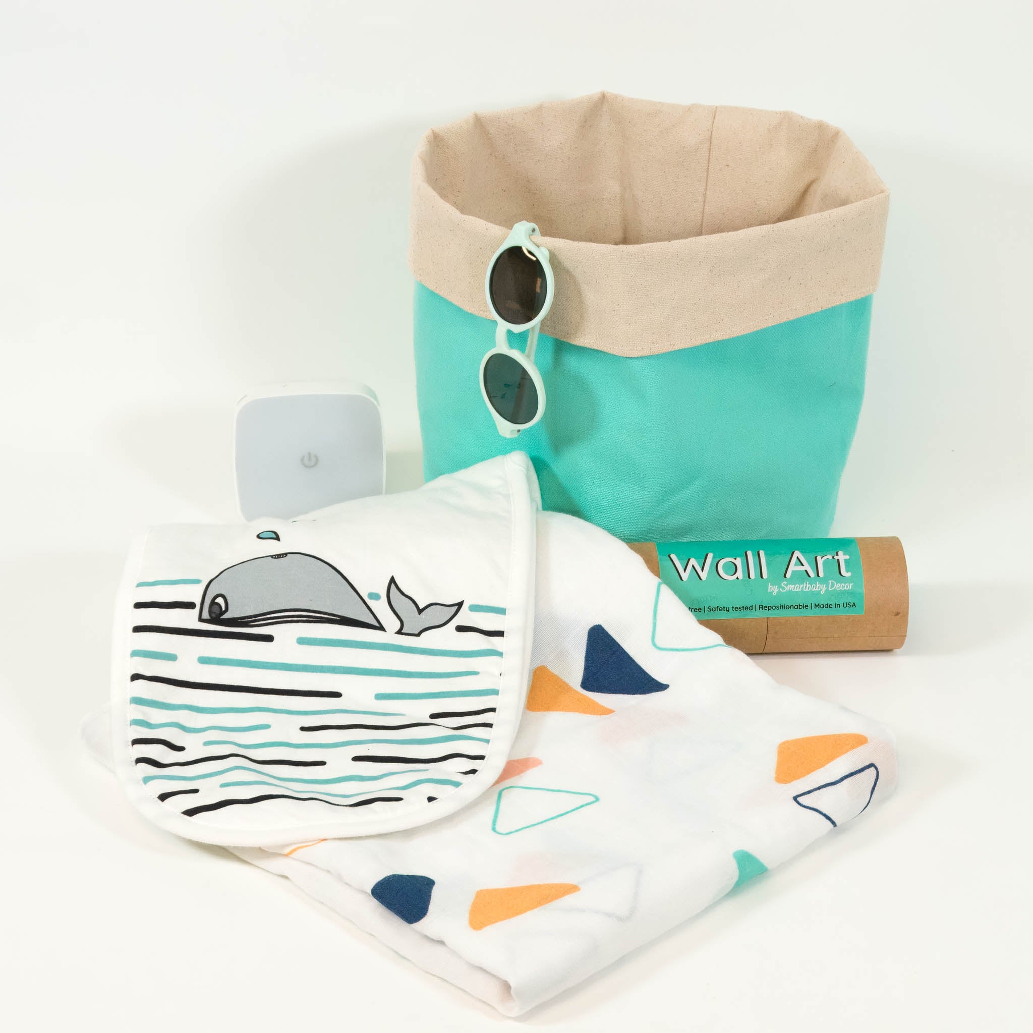 The contents of the Smartbaby Baby Shower Box are displayed including: infant sunglasses, a storage basket, night light, wall art, burp cloth and blanket. 