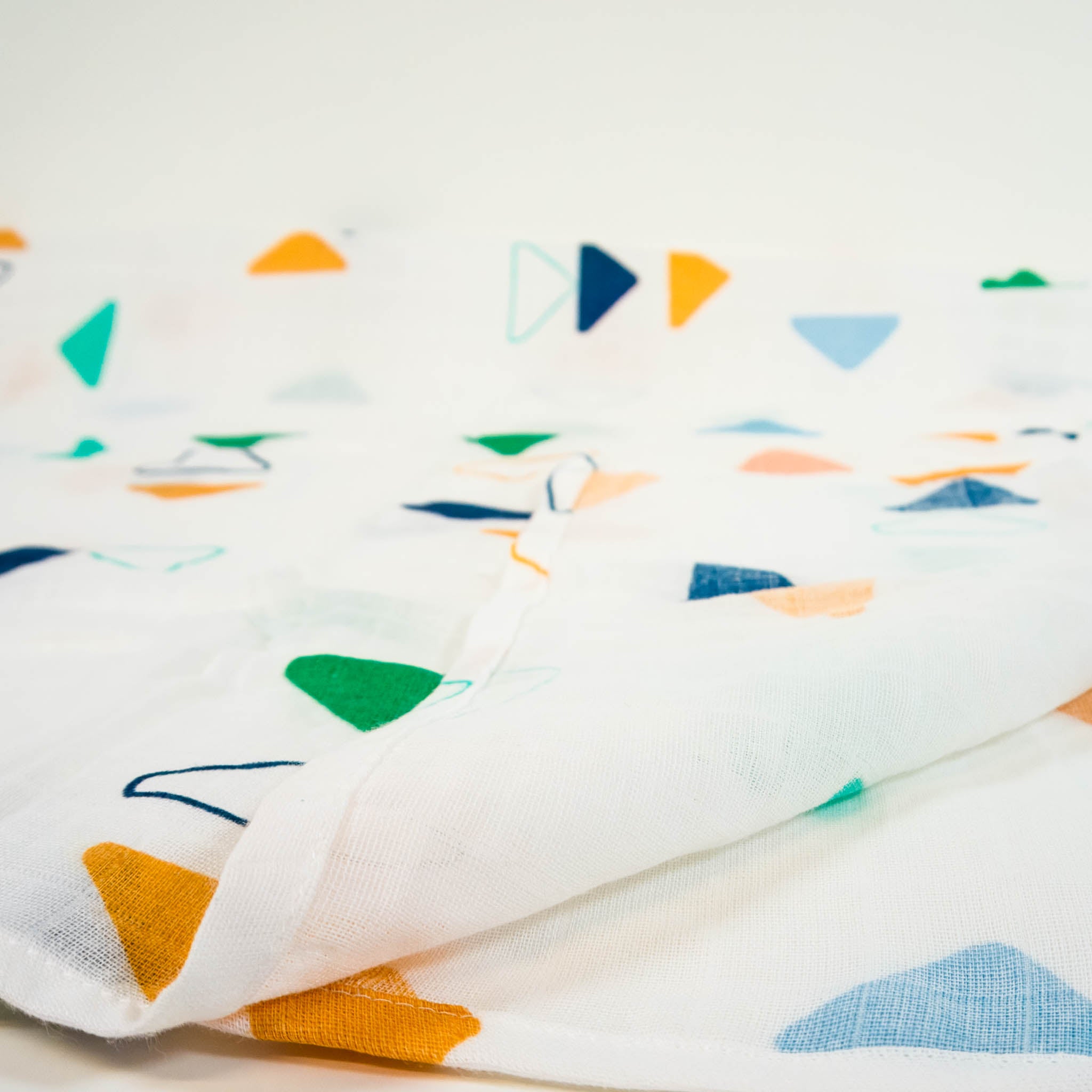 A zoomed in view of a muslin cotton blanket that is white with colorful triangles all over. 