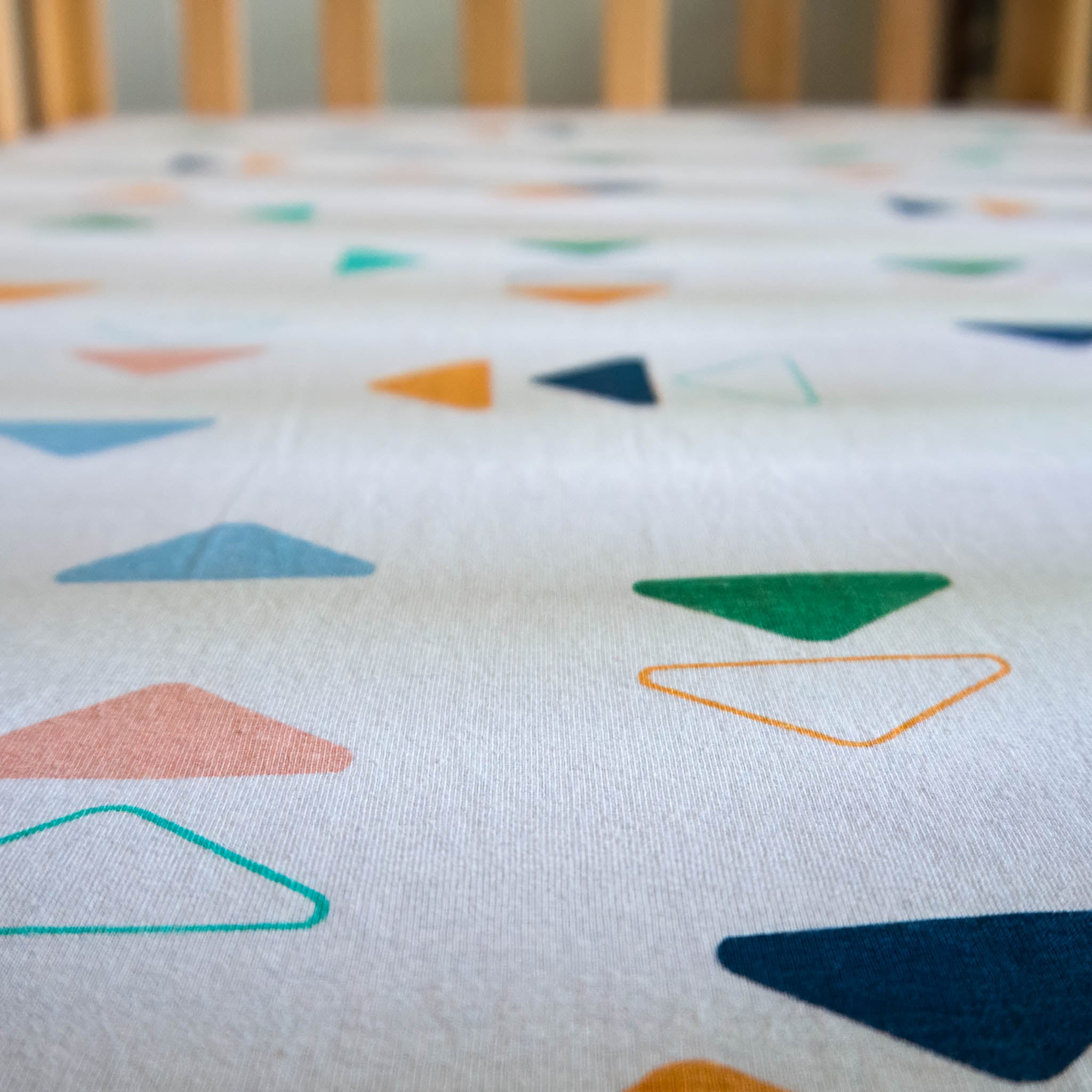 A zoomed in view of a white crib sheet with a scattered triangle pattern in multiple colors. 