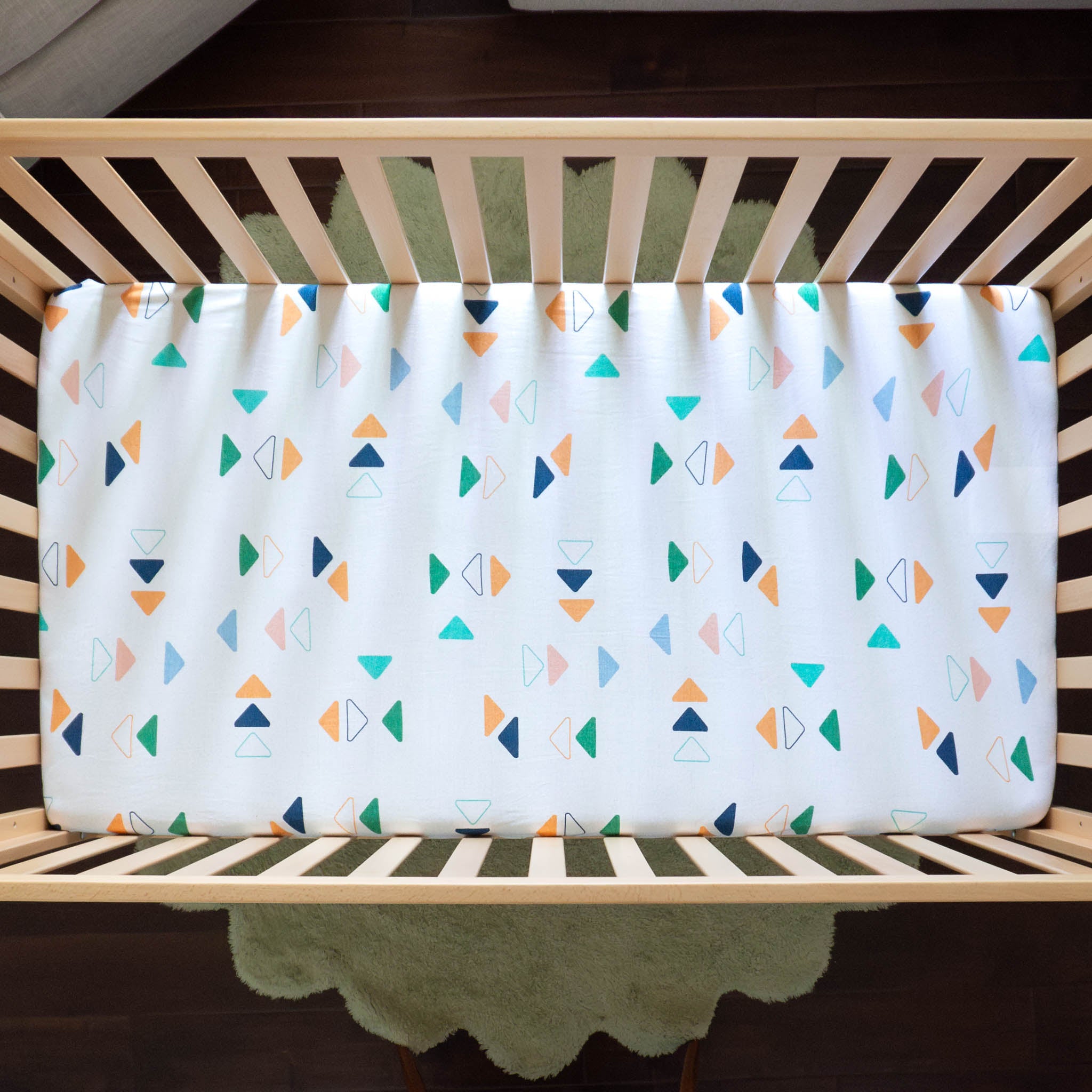 An aerial view of a white crib sheet with a repeated triangle pattern in different colors. 