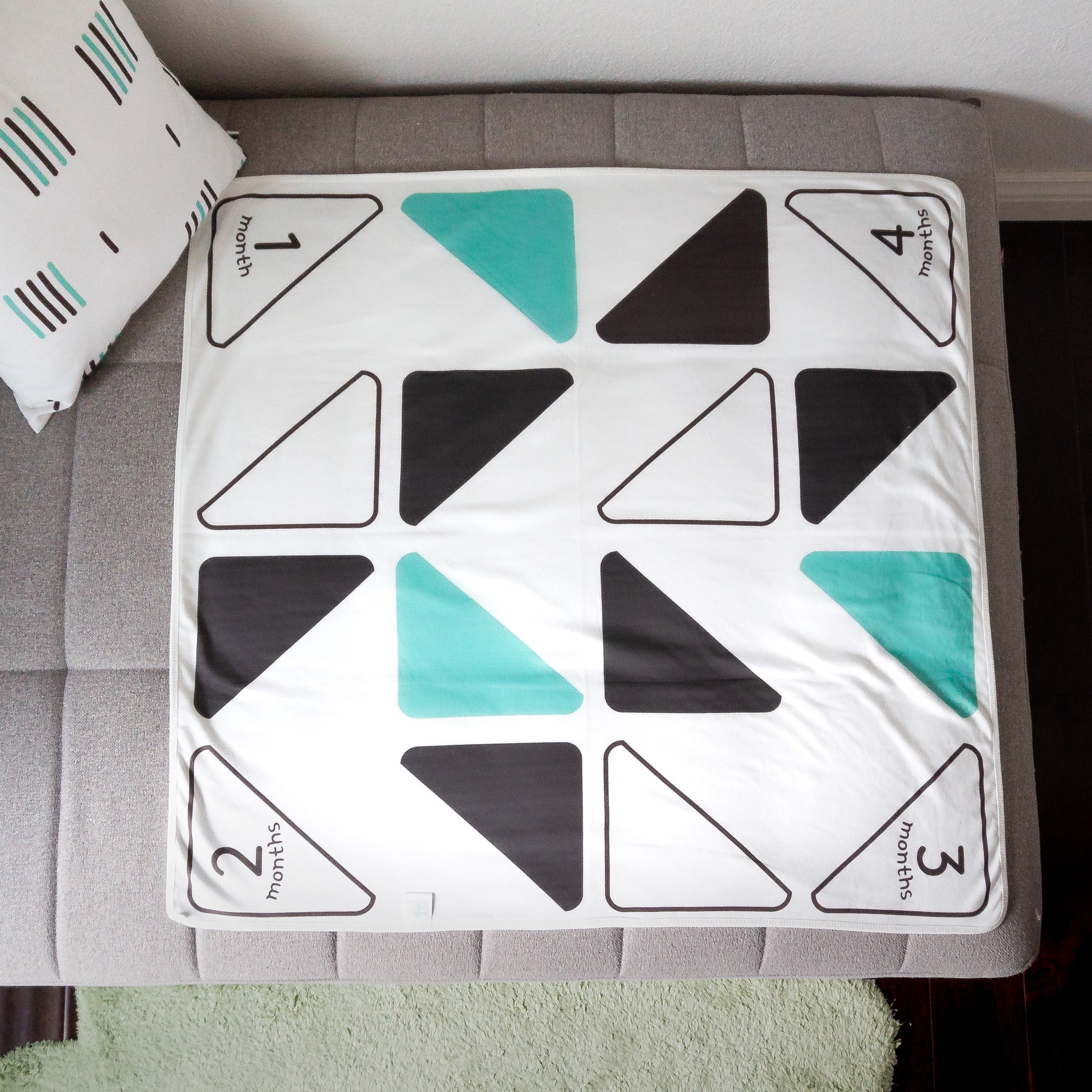 A baby blanket with black, mint green and white triangles displayed on a chaise sofa. 