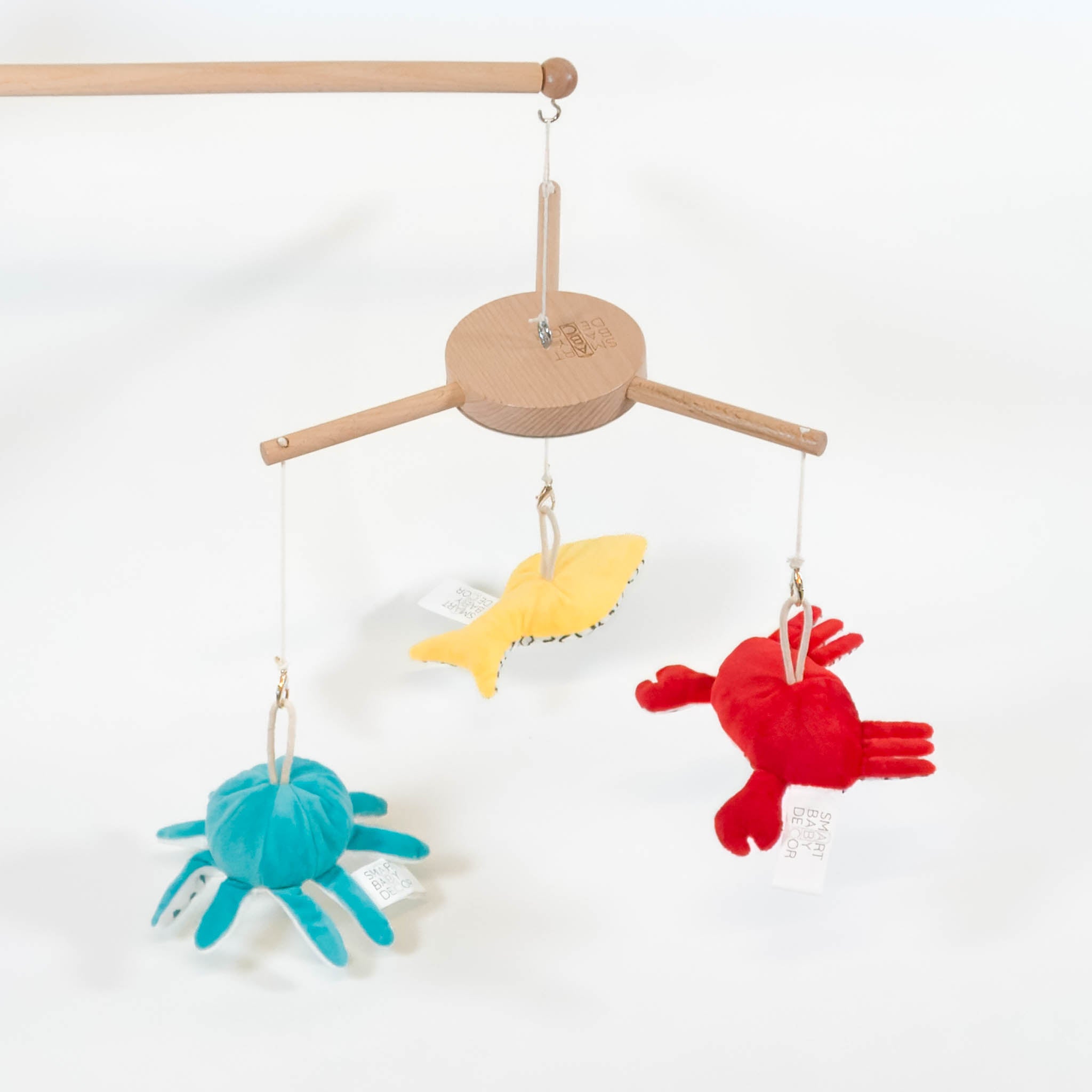 A baby's mobile with a wooden arm and three ocean characters in different colors: a yellow fish, blue octopus and red crab.