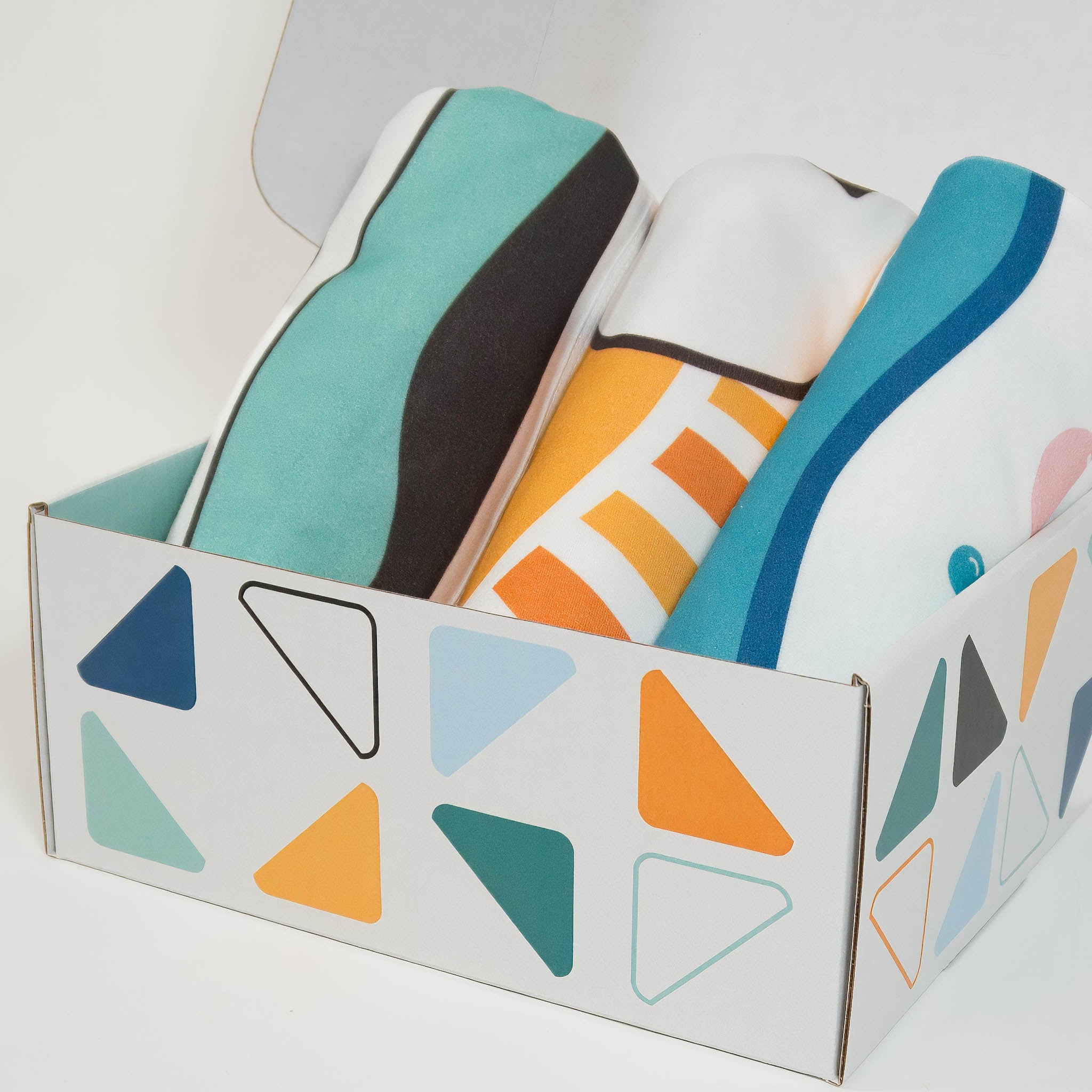 A box with a triangle pattern on the outside is shown with three rolled up organic cotton blankets. 