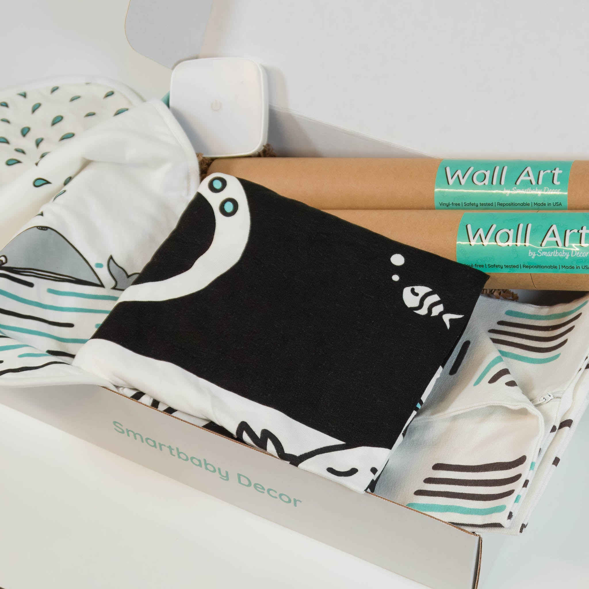 An open box showing contents of the bundle, including tubes of wall stickers, a burp cloth with a whale print, black and white crib sheet, throw pillow cover and night light.