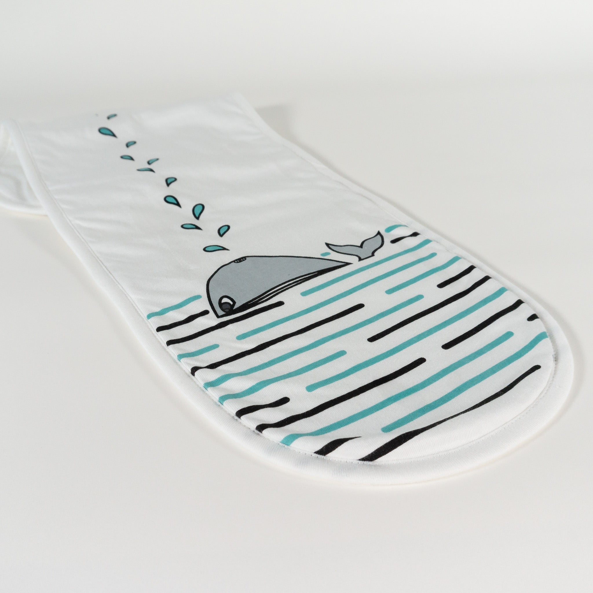 A baby's burp cloth in white organic cotton laid out with a print of a whale.