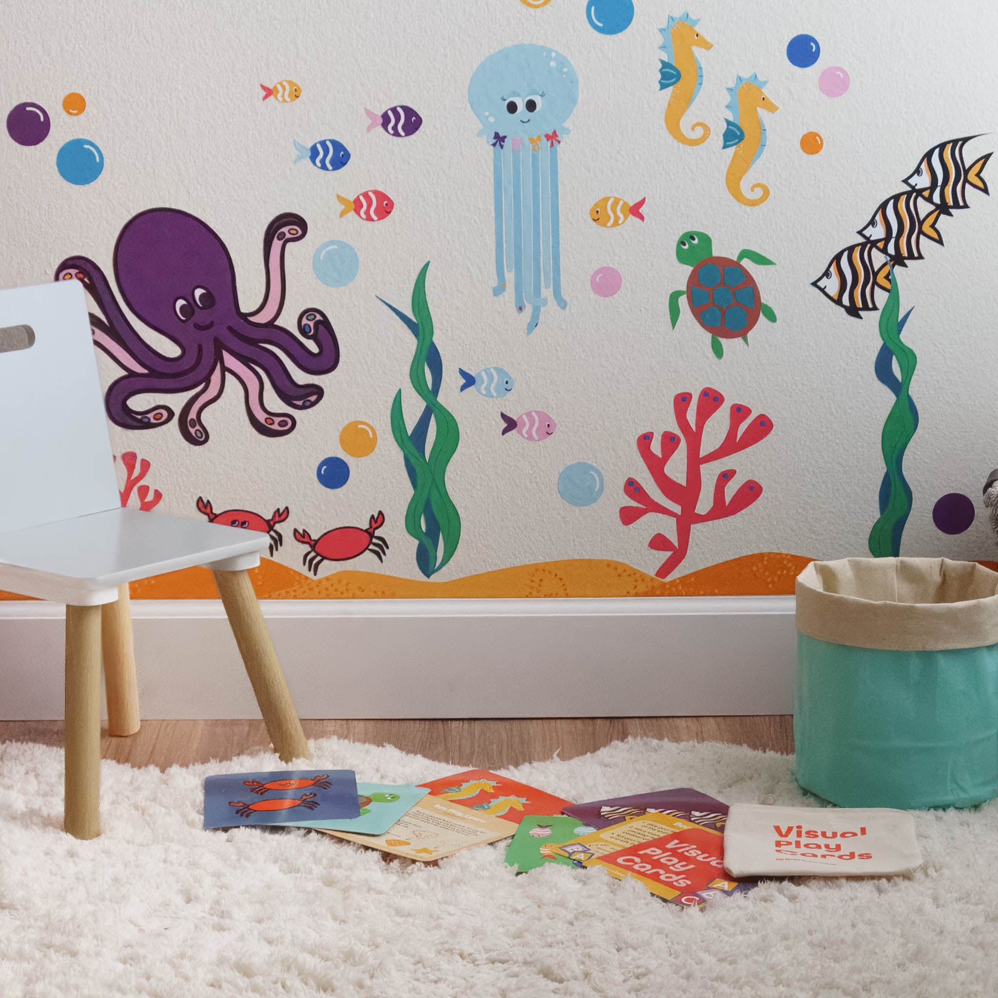 A colorful ocean mural on a white wall made with wall stickers, a storage basket and colorful activity cards are on the floor in front.