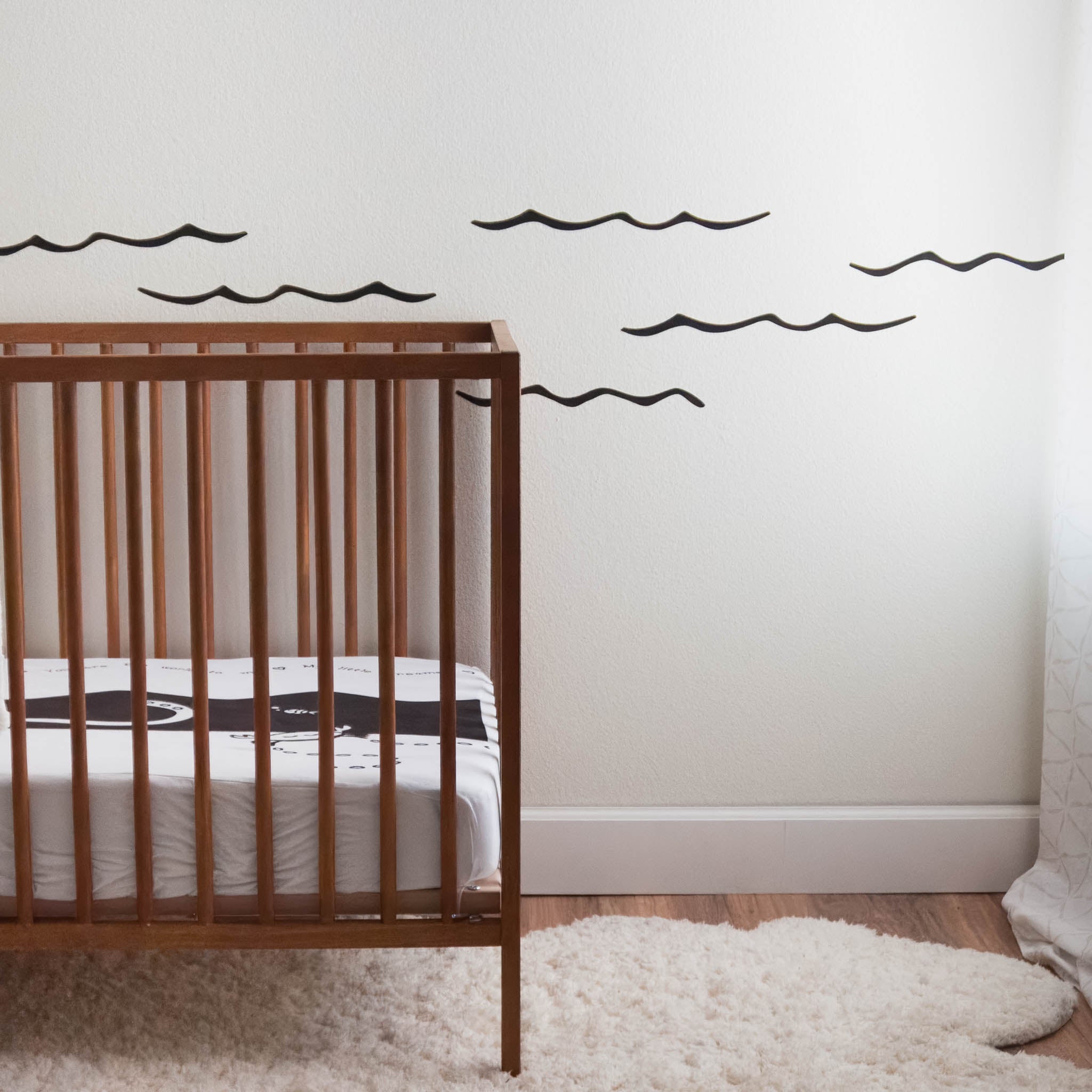 A white wall with black ocean waves wall stickers. In front is a wooden crib.