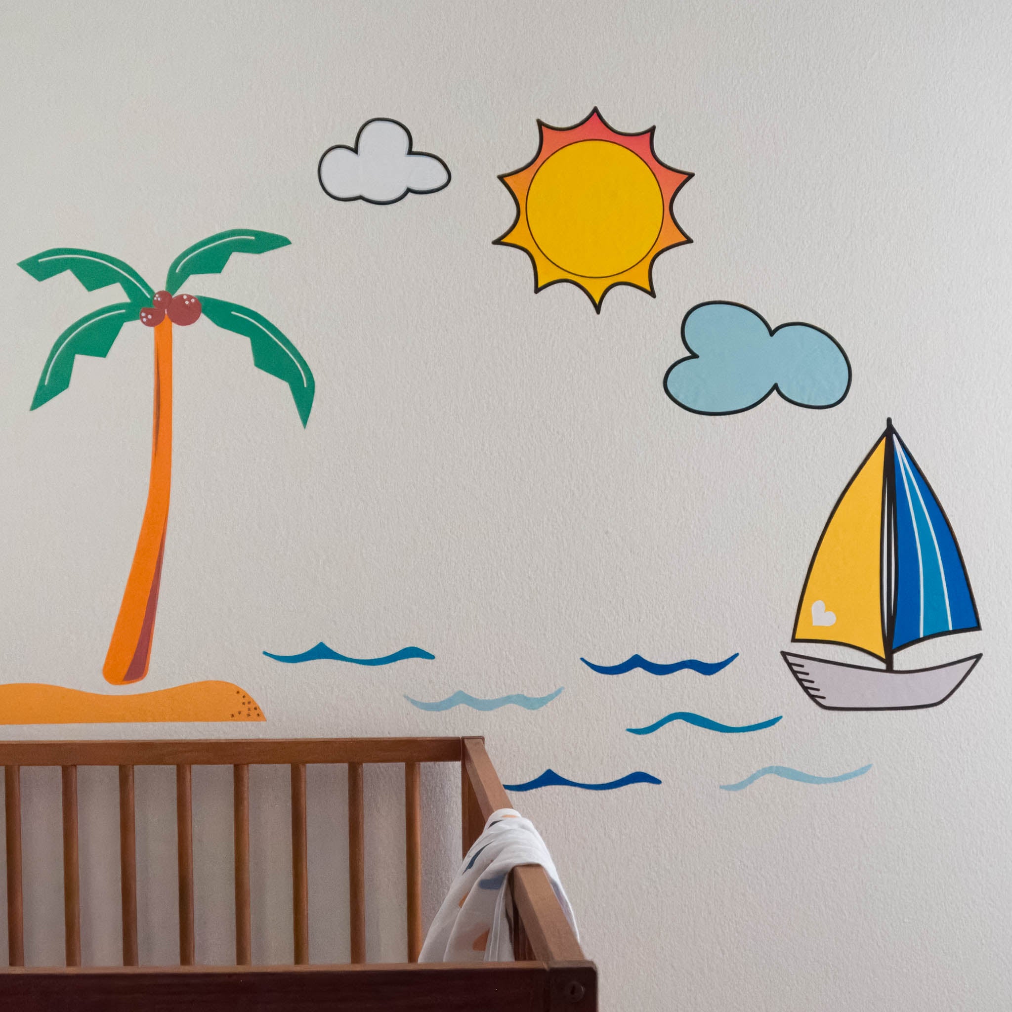 A topical ocean scene including a coconut tree, sun and clouds, sailboat and blue waves on a white wall with the edge of a wooden crib visible.