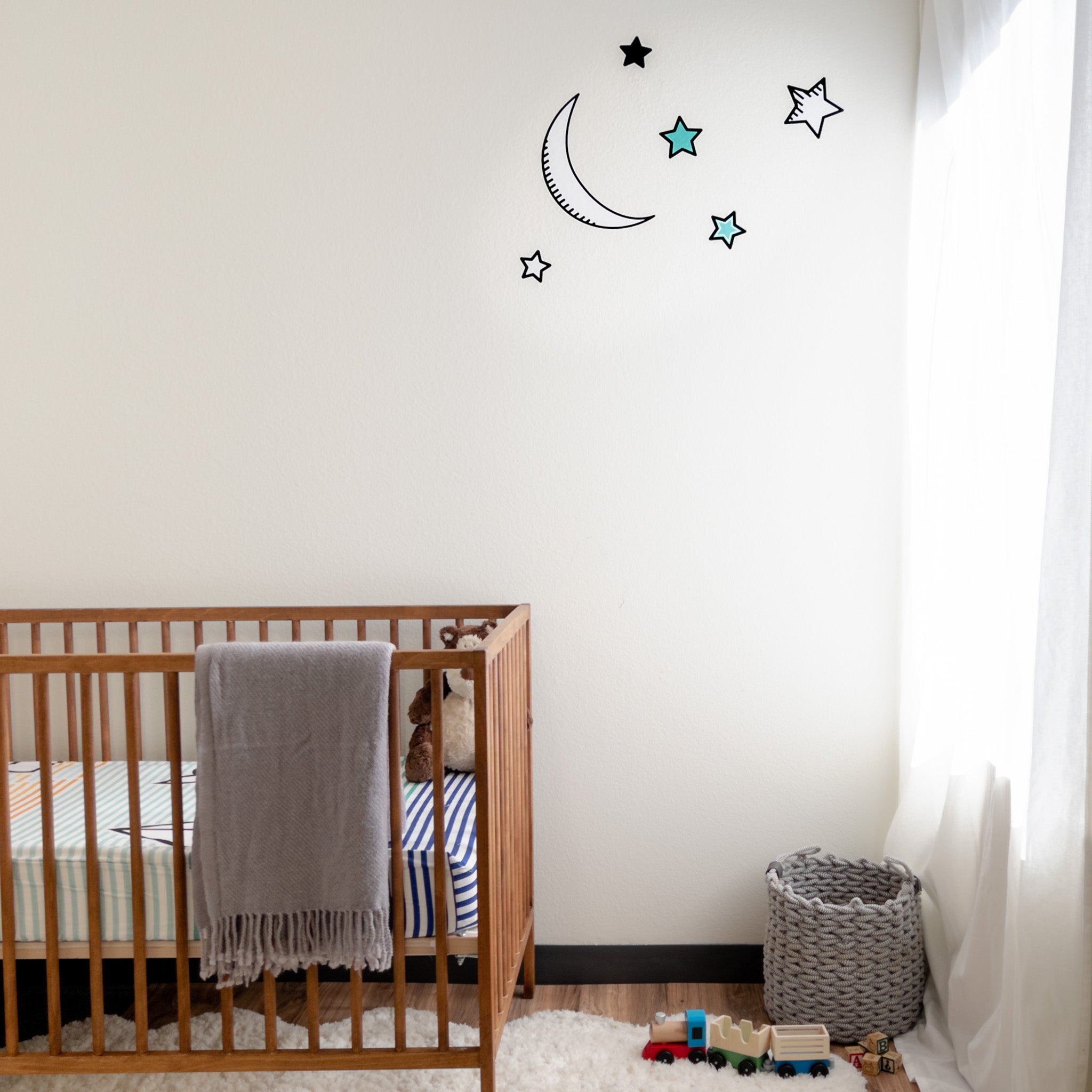 A nursery room with a crib on the left side, a window on the right and moon and stars wall decal set on the wall.