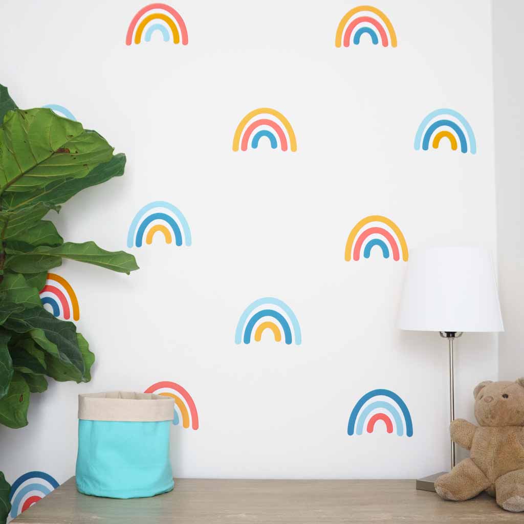 Wall of scattered rainbow decals with velvet arches, with teddy bear, lamp, storage basket and plant in front