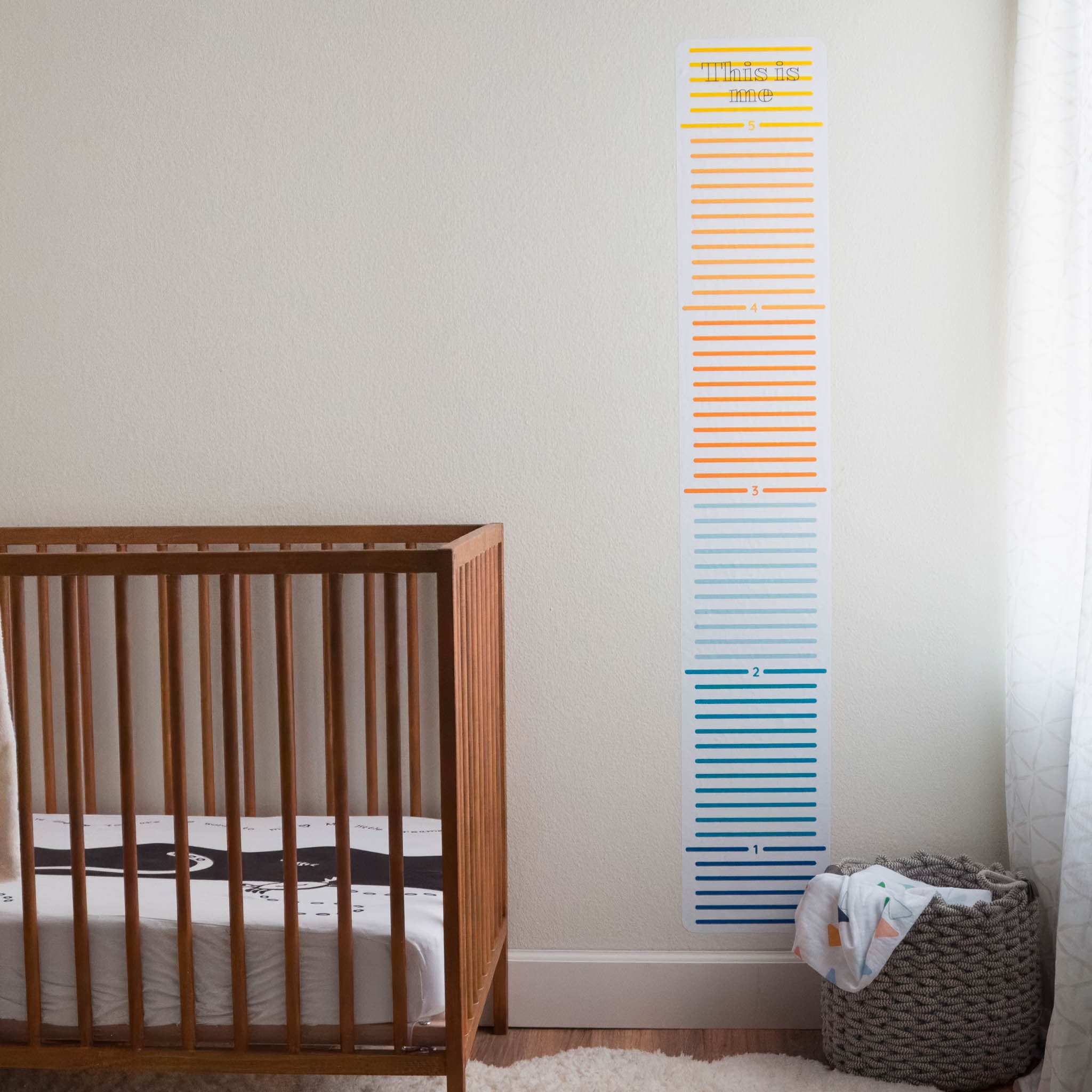 A nursery with a window on the right side, crib on the left and a colorful child's growth chart on the wall in between.