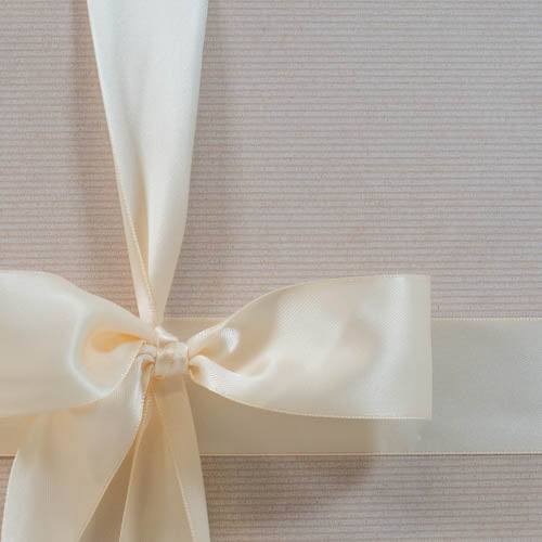 A close up of an ivory satin ribbon bow on a gift box wrapped with a neutral light beige paper.