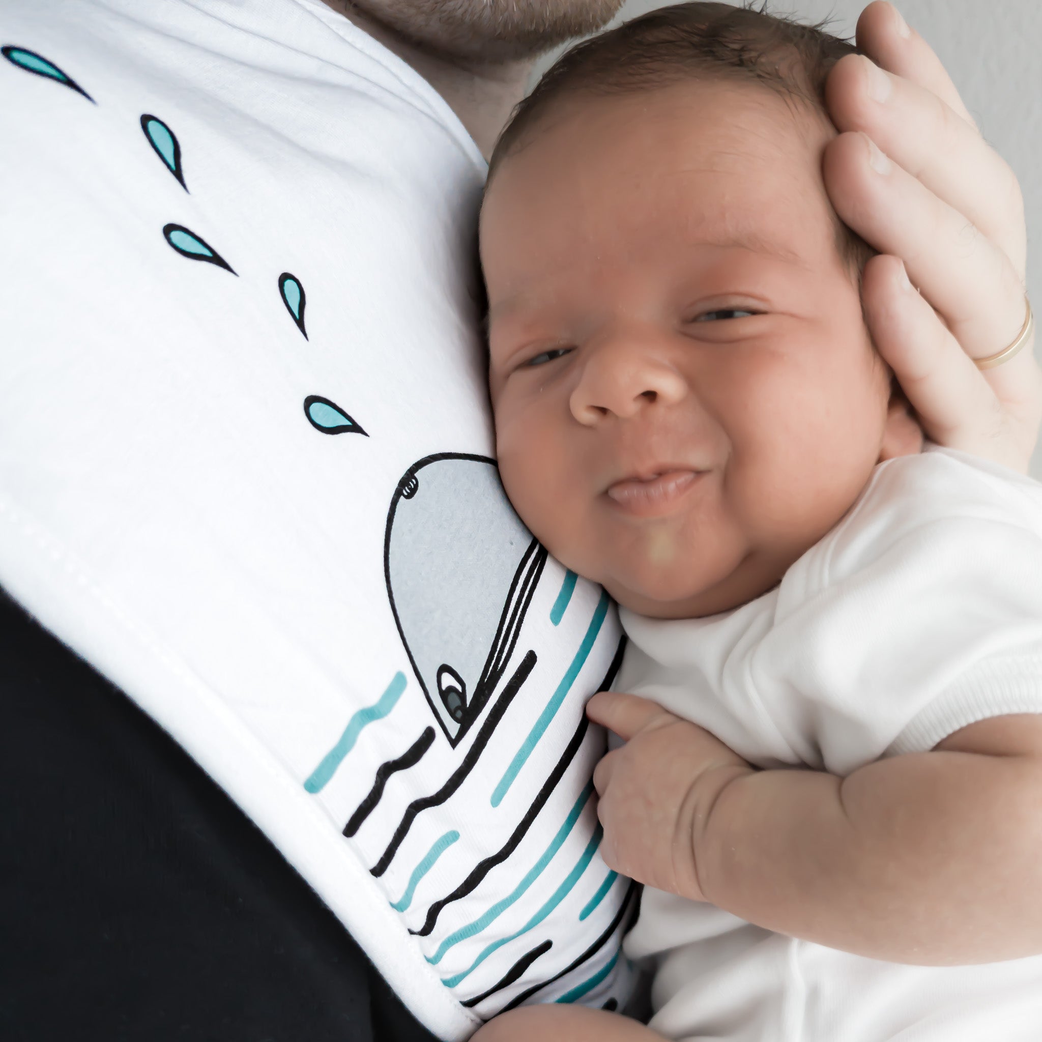 A baby being held up against a white burp cloth with a whale pattern on it.