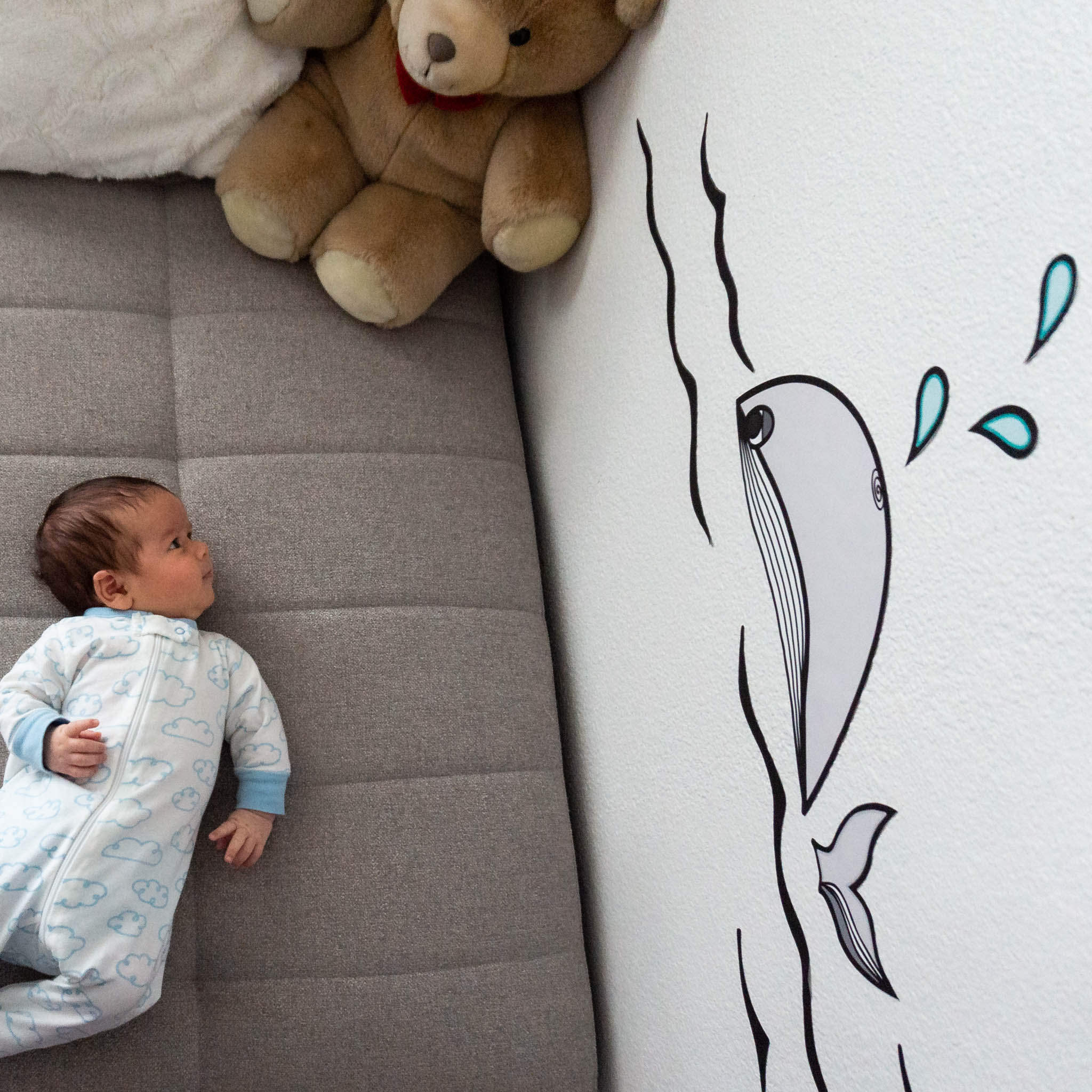 A newborn baby on the left looking at a wall decal of a whale in a black and white pattern.