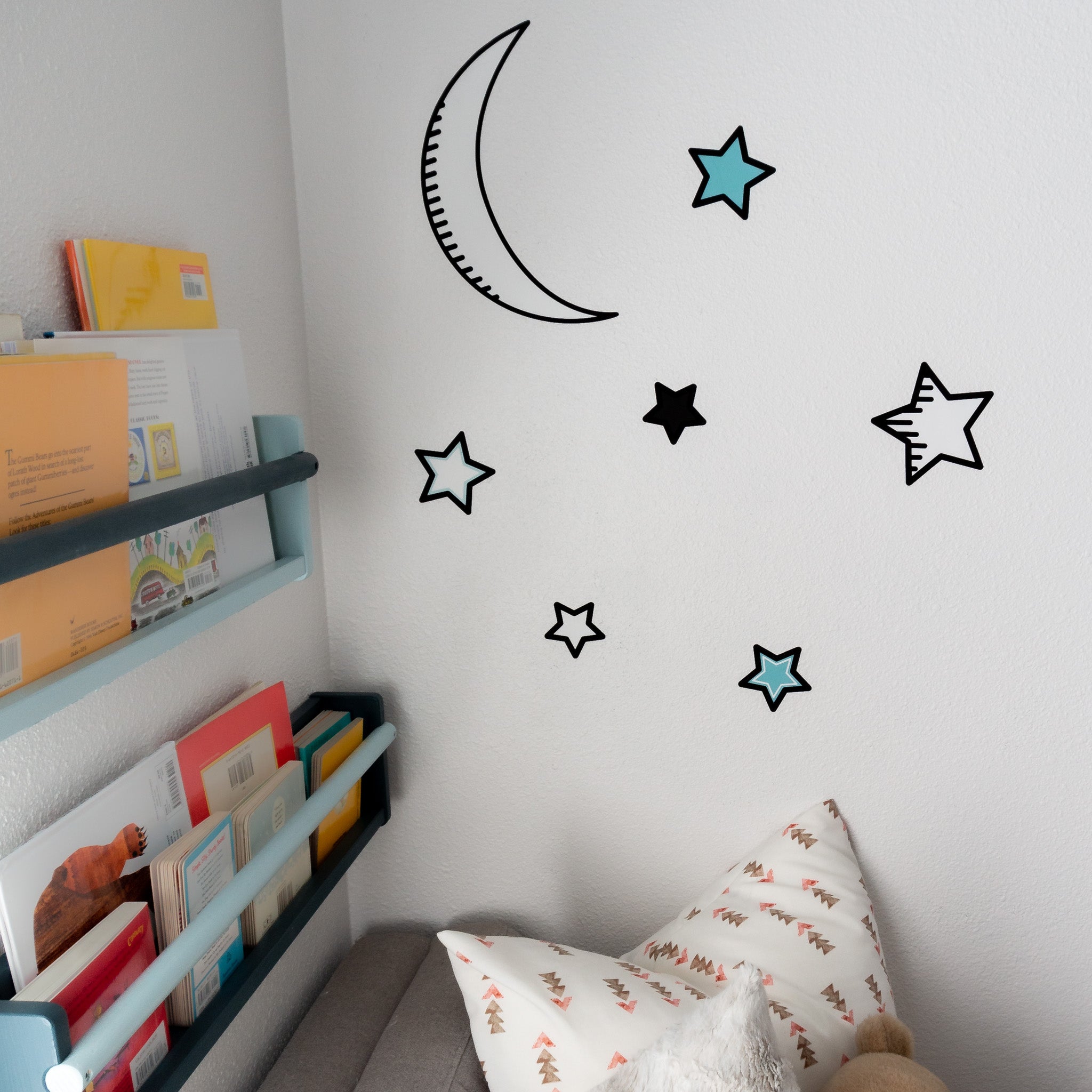 The corner of a child's room, with bookshelves on the left and moon and star wall decals on the wall.